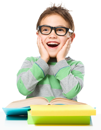 Astonished little boy is reading a book while wearing glasses, isolated over whiteの写真素材