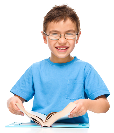 Cute little boy is reading a book while wearing glasses, isolated over whiteの写真素材