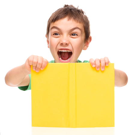 Little boy is holding a book and showing aggressive grimace, isolated over whiteの写真素材