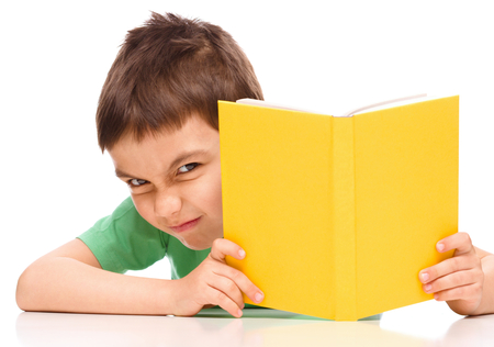 Cute little boy plays with book while sitting at table, isolated over whiteの写真素材