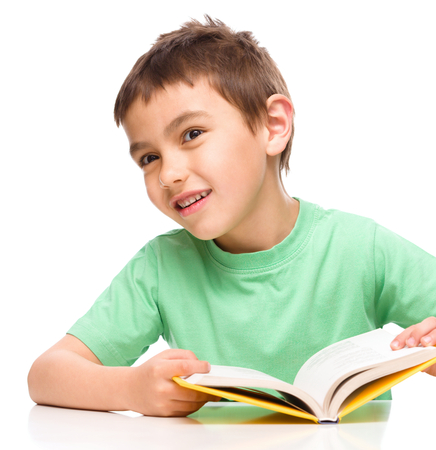 Cute little child plays with book while sitting at table, isolated over whiteの写真素材