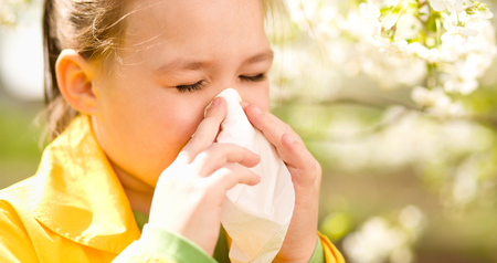 Little girl is blowing her nose near spring tree in bloomの写真素材