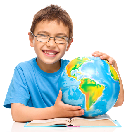 Little boy is examining globe while sitting at table, isolated over whiteの写真素材