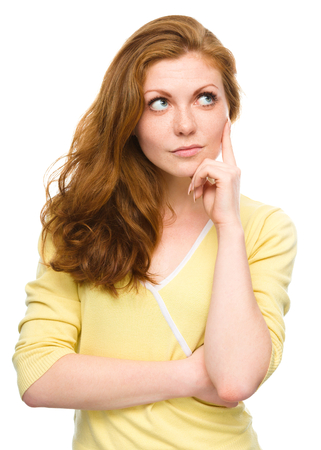 Portrait of a happy young woman thinking about something while touching her cheek with finger, isolated over whiteの写真素材
