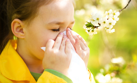 Little girl is blowing her nose near spring tree in bloomの写真素材