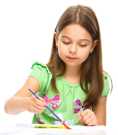 Little girl is painting with gouache while sitting at table, isolated over whiteの写真素材