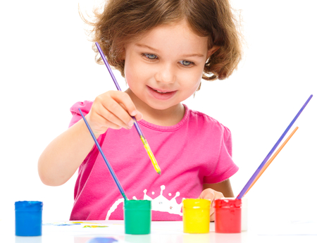 Little girl is painting with gouache while sitting at table, isolated over whiteの写真素材