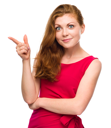 Portrait of a young woman pointing to the left using her index finger, isolated over whiteの写真素材