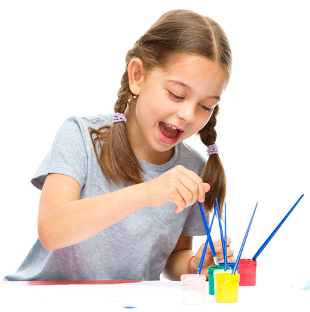 Little girl is painting with gouache while sitting at table, isolated over whiteの写真素材
