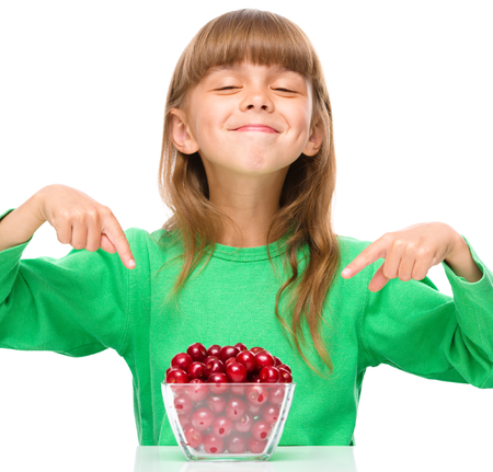 Cute girl is pointing to the bowl full of cherries, isolated over whiteの写真素材