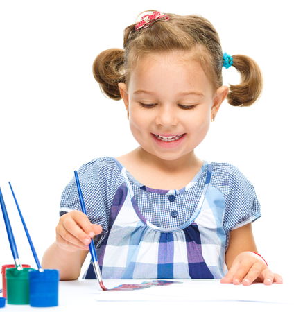 Little girl is painting with gouache while sitting at table, isolated over whiteの写真素材