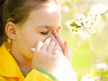 Little girl is blowing her nose near spring tree in bloomの写真素材