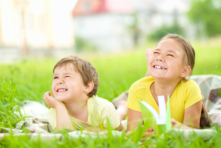 Little girl and boy are playing outdoors while laying on green grassの写真素材