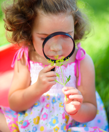 Young girl is looking at flower through magnifier, outdoor shootの写真素材