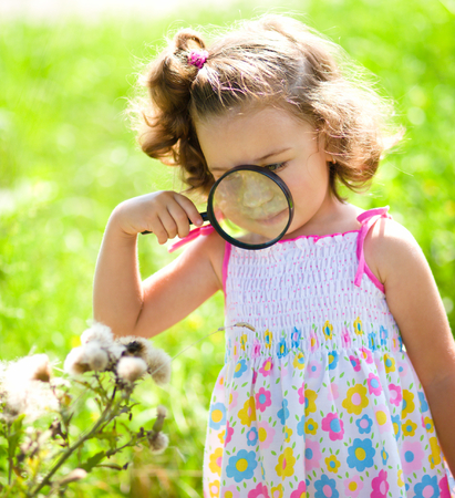 Young girl is looking at flower through magnifier, outdoor shootの写真素材