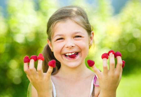 Young girl is holding raspberries on her fingers, outdoor shootの写真素材