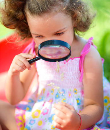 Young girl is looking at flower through magnifier, outdoor shootの写真素材