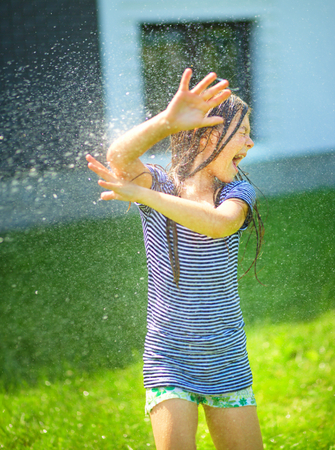 Happy girl is playing under rain on backyardの写真素材