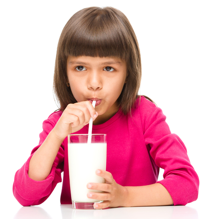 Cute little girl drinks milk using drinking straw, isolated over whiteの写真素材