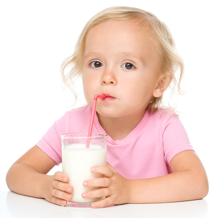 Cute little girl drinks milk using drinking straw, isolated over whiteの写真素材