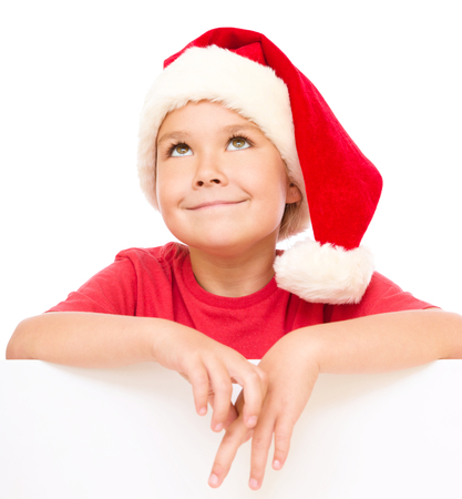 Little girl in santa hat is holding blank board and smiling, isolated over whiteの写真素材