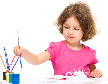Little girl is painting with gouache while sitting at table, isolated over whiteの写真素材