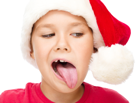 Little girl in santa hat is trying to touch the pompon with her tongue, isolated over whiteの写真素材