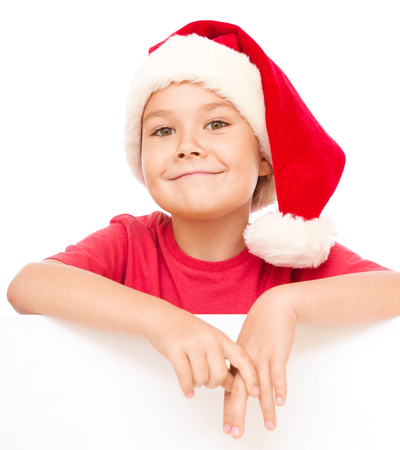 Little girl in santa hat is holding blank board and smiling, isolated over whiteの写真素材