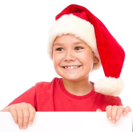 Little girl in santa hat is holding blank board and smiling, isolated over whiteの写真素材