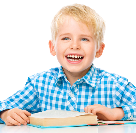 Cute little child play with book while sitting at table, isolated over whiteの写真素材