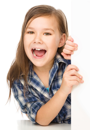 Little girl is looking from out blank board and showing thumb up sign, isolated over whiteの写真素材