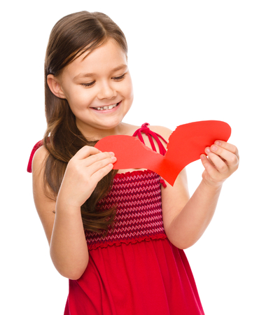 Portrait of a happy little girl tearing red heart apart, valentine concept, isolated over whiteの写真素材