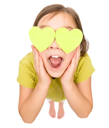 Little girl is holding hearts over her eyes, fisheye portrait, valentine concept, isolated on whiteの写真素材