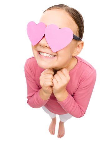 Little girl is holding hearts over her eyes, fisheye portrait, valentine concept, isolated on whiteの写真素材