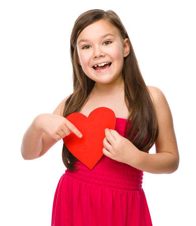 Portrait of a little girl holding red heart and pointing to it using index finger, isolated over whiteの写真素材