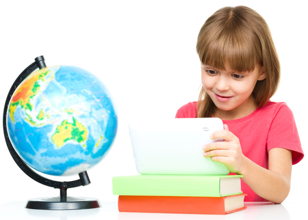 Young girl is using tablet while sitting at table, isolated over whiteの写真素材