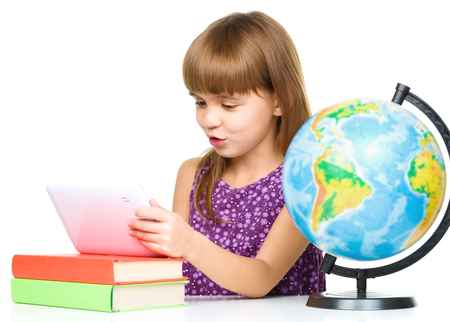 Surprised young girl is using tablet while studying geography, isolated over whiteの写真素材