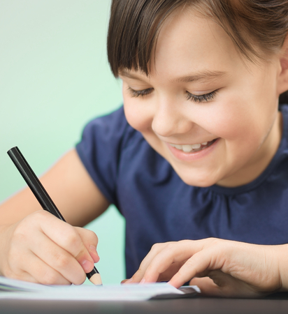 Cute cheerful child drawing using pencil while sitting at table, closeupの写真素材