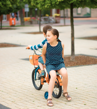 Two children, sister and brother, are riding same bicycle outdoorsの写真素材