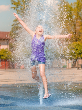 Hot summer in the city - girl is jumping through fountain with cold waterの写真素材
