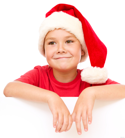 Little girl in santa hat is holding blank board and smiling, isolated over whiteの写真素材