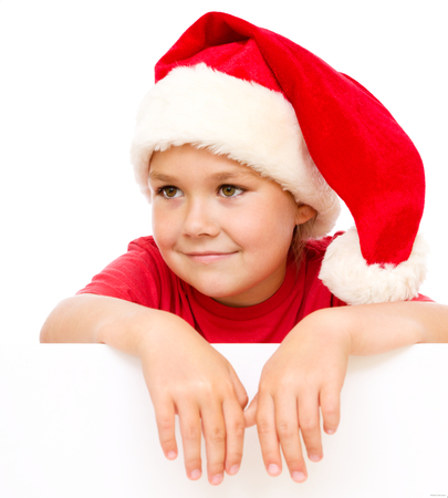 Little girl in santa hat is holding blank board and smiling, isolated over whiteの写真素材