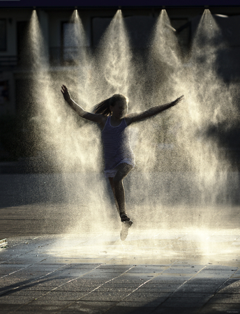 Hot summer in the city - girl is enjoying spray installation with cold waterの写真素材