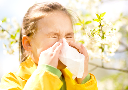 Little girl is blowing her nose near spring tree in bloomの写真素材