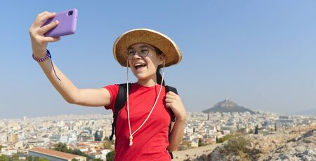Girl is taking selfies in Athens, Greece using smartphone, view on mount Lycabettus, outdoor shootの写真素材