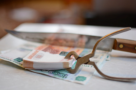 Russian currency is squeezed with pliers and cut with a knife on a blurred backgroundの写真素材