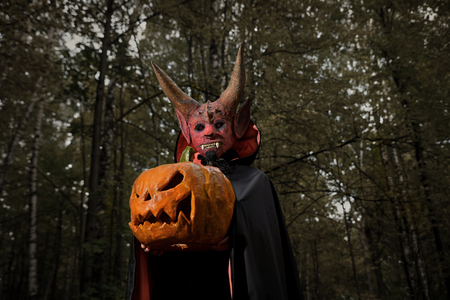 Devil in the dark forest with a pumpkin for Halloween in the hands