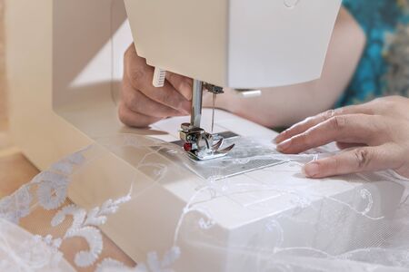 Seamstress sews a white curtain on a sewing machine. Work wizard in sewing fabrics. Steel needle...
