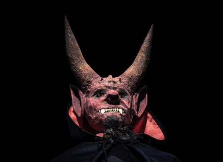Devil with horns and in a black cloak on a dark background looks up. Man in scary mask for halloween.の写真素材