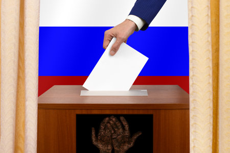 Fake polling station in Russia. A man puts a ballot paper into a fake ballot box against the background of the Russian flag. Electoral interference.の写真素材
